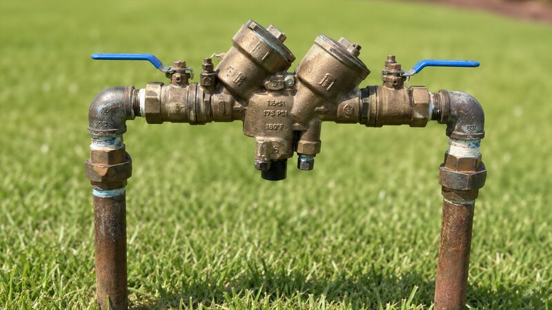 Brass reduced pressure backflow prevention assembly with blue shutoff handles, installed on risers above a residential lawn