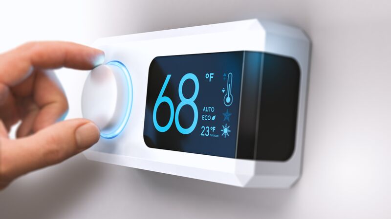 Hand adjusting a modern smart digital thermostat displaying 68°F